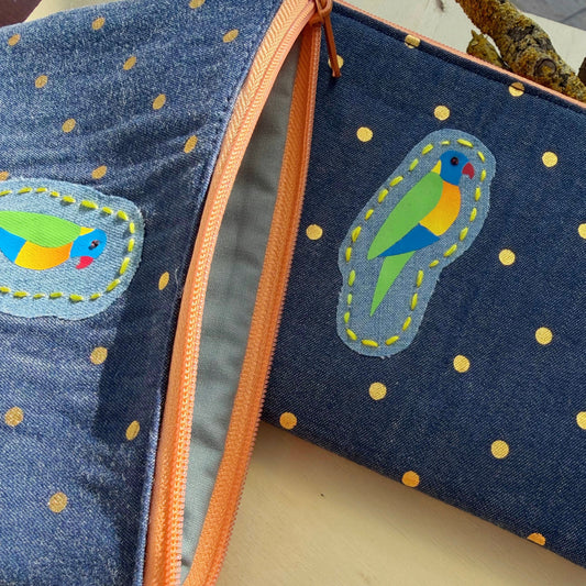 Blue denim pouch with bird appliqués and orange zipper on a light background