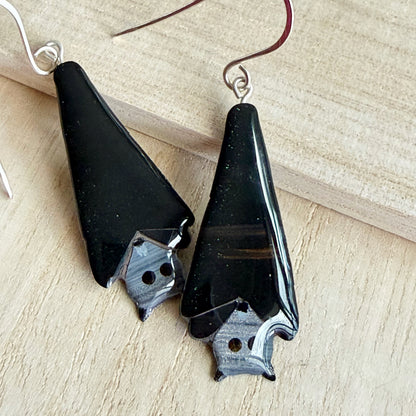 A pair of black grey-headed flying fox earrings with silver earring hooks on a wooden background 